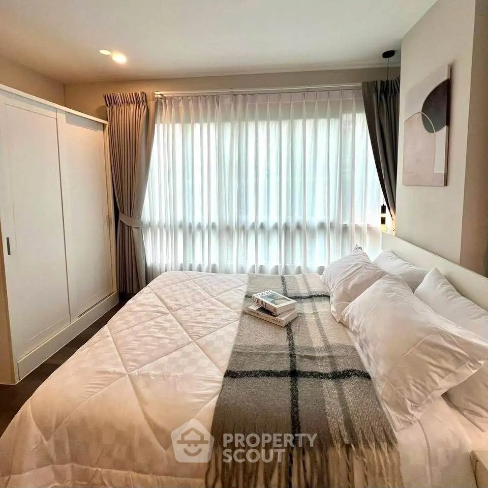 Spacious bedroom with large window and elegant decor, featuring a cozy bed and ample natural light.