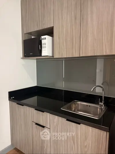 Modern kitchen with sleek cabinetry and built-in microwave, featuring a compact sink and glossy backsplash.
