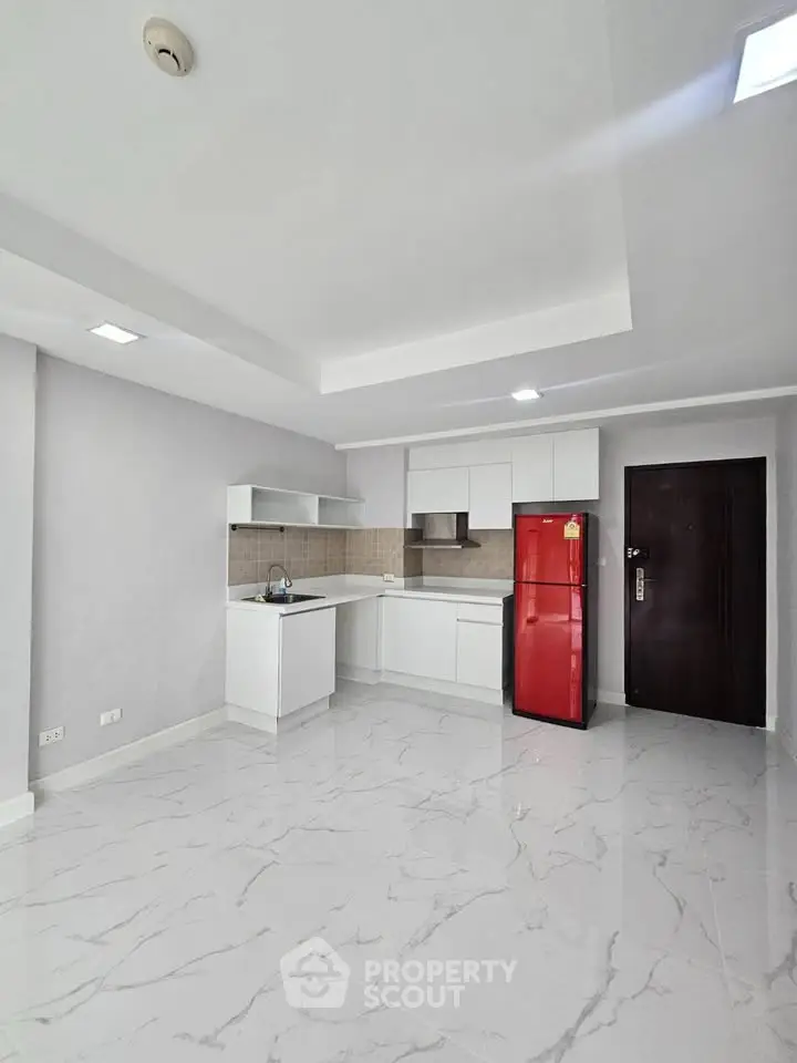 Modern kitchen with sleek white cabinetry and red refrigerator in a bright, spacious apartment.