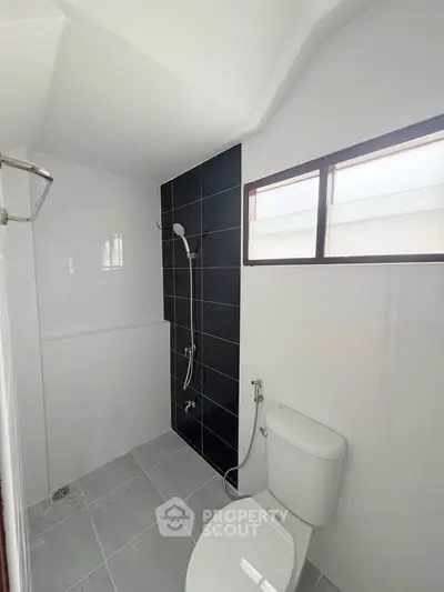 Modern minimalist bathroom with sleek black tile shower and white fixtures.