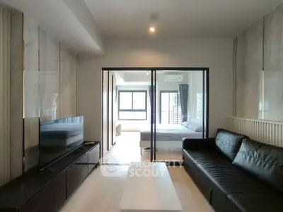 Modern living room with sleek black leather sofa and large TV, leading to a bright bedroom.