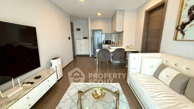 Modern living room with elegant decor and open kitchen layout, featuring a sleek TV setup and stylish furniture.