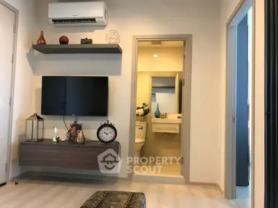 Modern living room with wall-mounted TV and view into a compact bathroom.