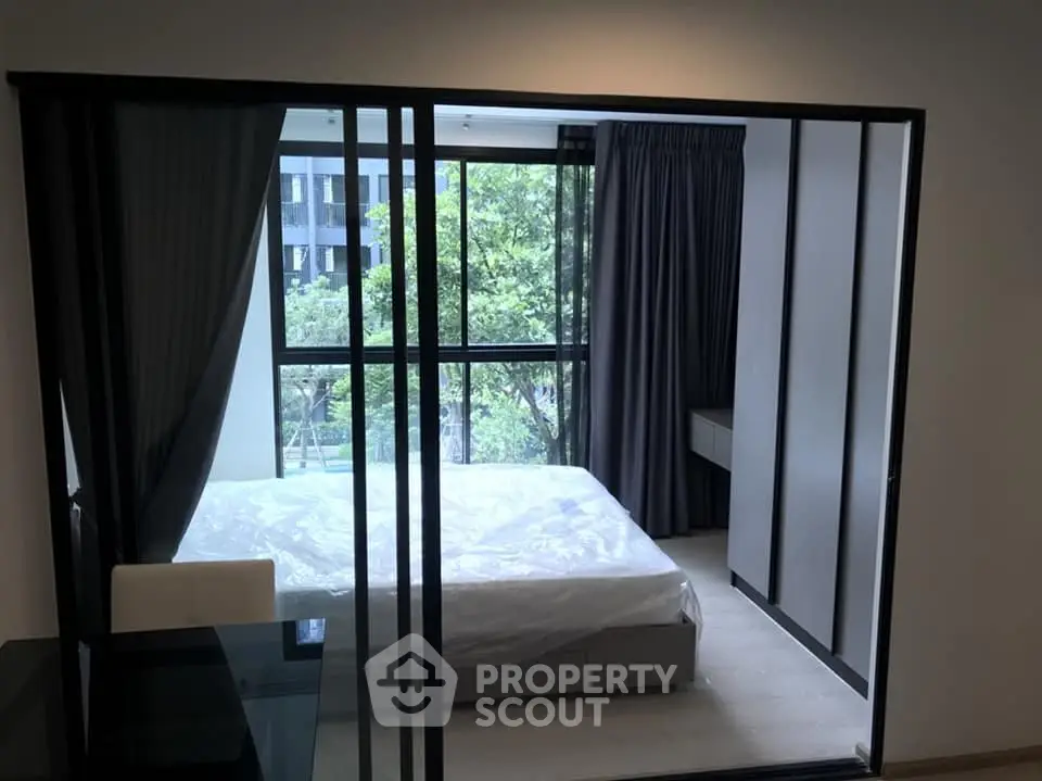 Modern bedroom with large window and sliding glass doors, offering a serene view.