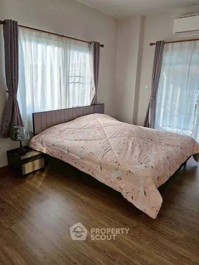 Cozy bedroom with large windows and elegant curtains, featuring a comfortable bed and wooden flooring.