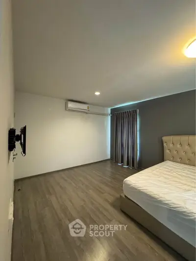 Spacious bedroom with modern flooring and elegant bed, featuring air conditioning and natural light.
