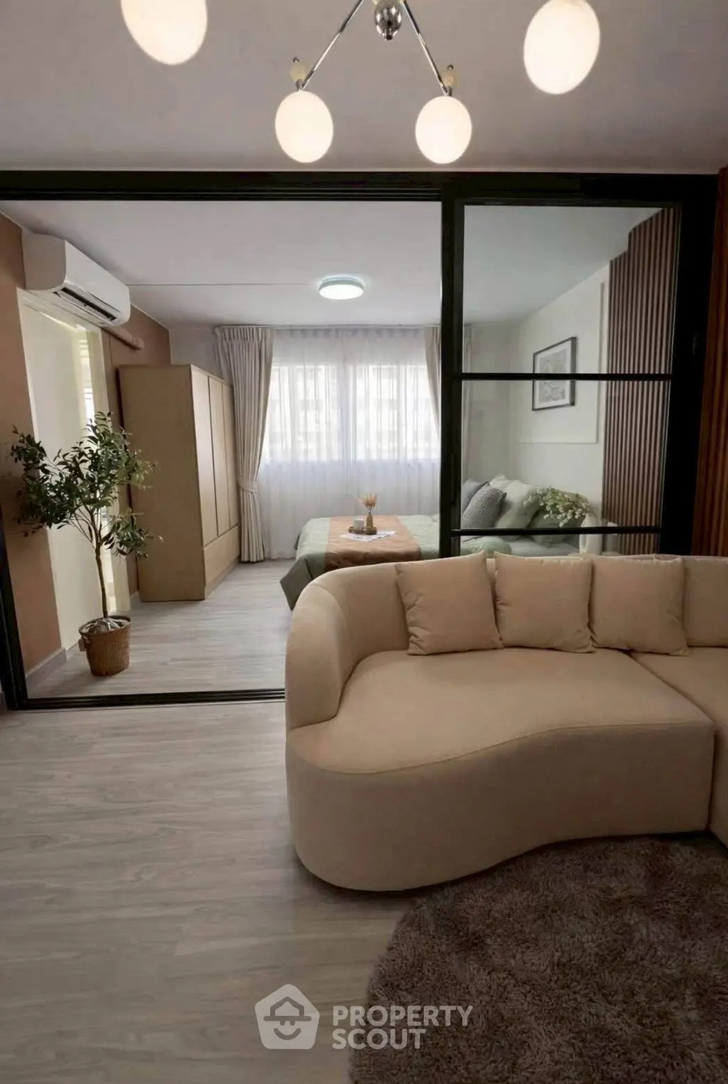 Modern living room with stylish sofa and view into cozy bedroom through glass partition.