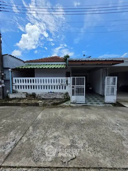 Charming single-story home with gated driveway and tiled roof under a bright blue sky.