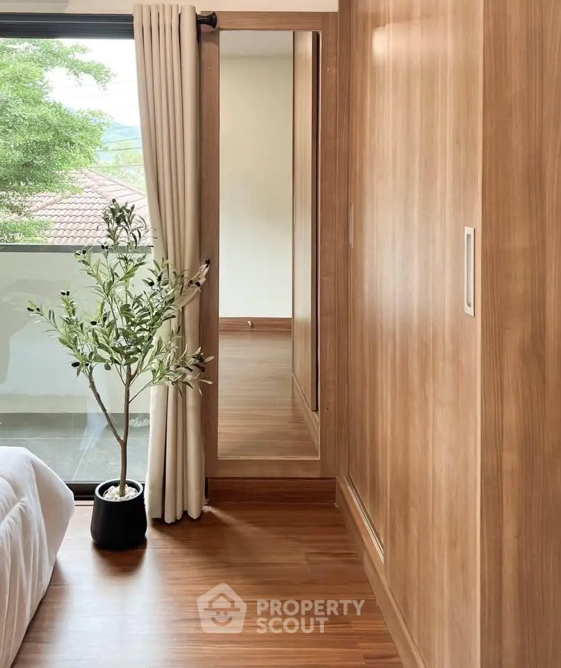 Elegant bedroom with wooden flooring, large window, and potted plant, offering a serene and natural ambiance.