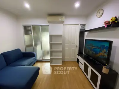 Cozy and inviting living space with sleek hardwood floors, modern air conditioning unit, and ample storage options, complemented by a large fridge and comfortable blue sofa set.