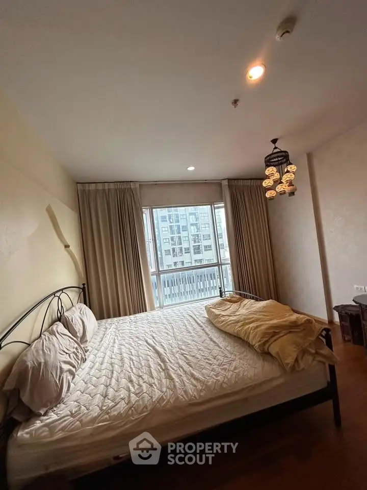 Cozy bedroom with large window and city view, featuring elegant lighting and neutral decor.