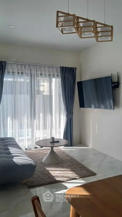 Modern living room with large window, stylish furniture, and wall-mounted TV
