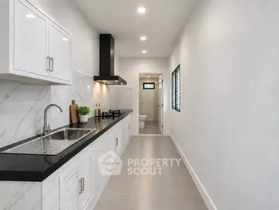 Sleek modern kitchen with black countertop and gas stove in a narrow layout.