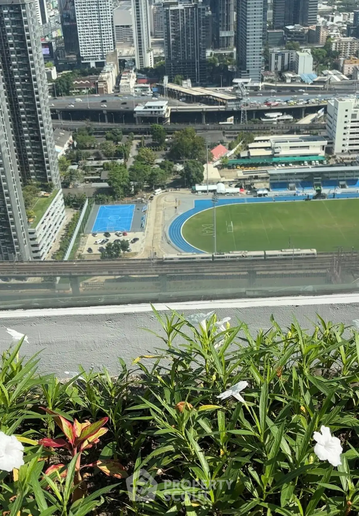 Stunning cityscape view from a high-rise balcony overlooking sports fields and urban skyline.