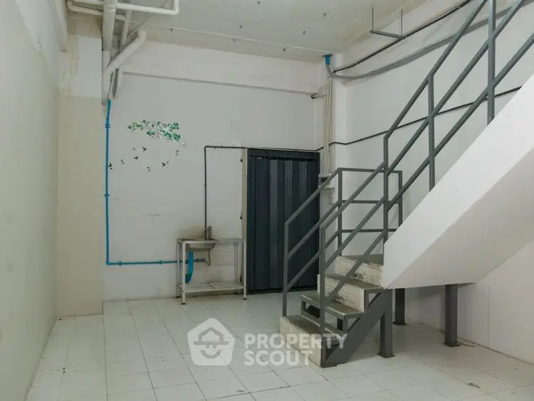 Industrial style interior with staircase and utility sink, ideal for storage or workspace.