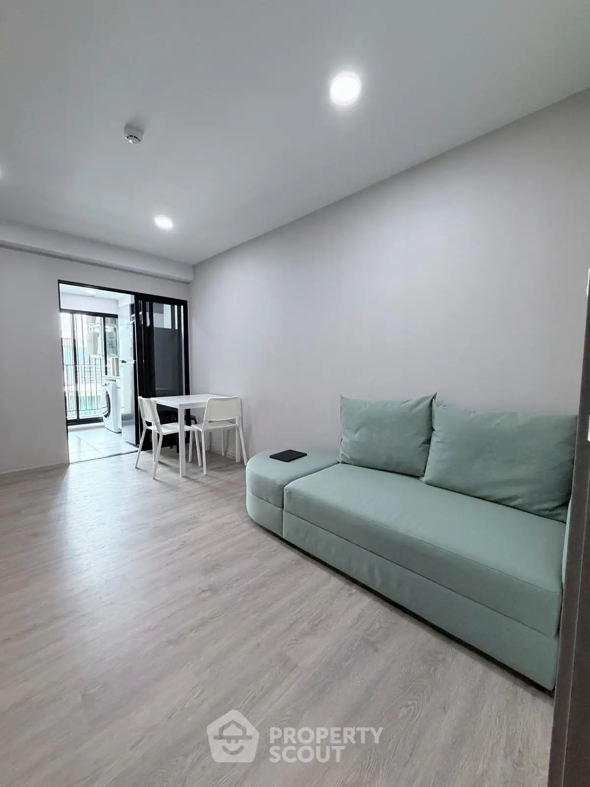 Modern living room with sleek sofa and dining area, featuring light wood flooring and balcony access.