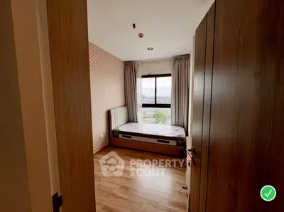 Cozy bedroom with wooden flooring and large window offering city view.