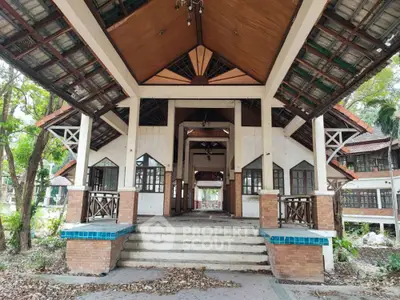 Charming rustic building entrance with wooden beams and tiled roof, surrounded by lush greenery.