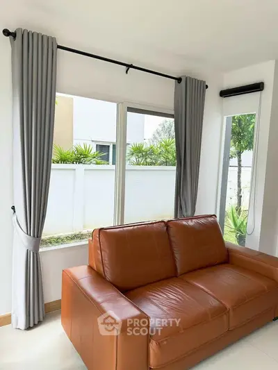 Modern living room with leather sofa and large windows offering garden view.