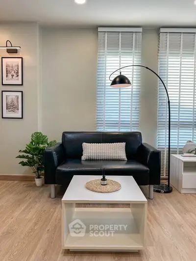 Modern living room with sleek black sofa, stylish floor lamp, and elegant decor in a cozy setting.