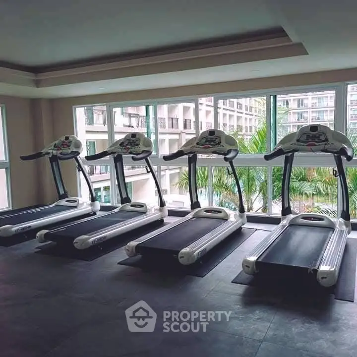 Modern gym with treadmills and large windows overlooking a scenic view in a luxury apartment complex.