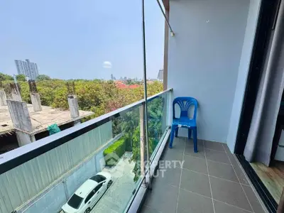 Spacious balcony with glass railing offering a serene view of greenery and cityscape.