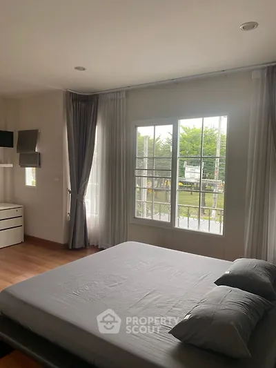 Spacious bedroom with large window and modern furnishings, offering a serene garden view.
