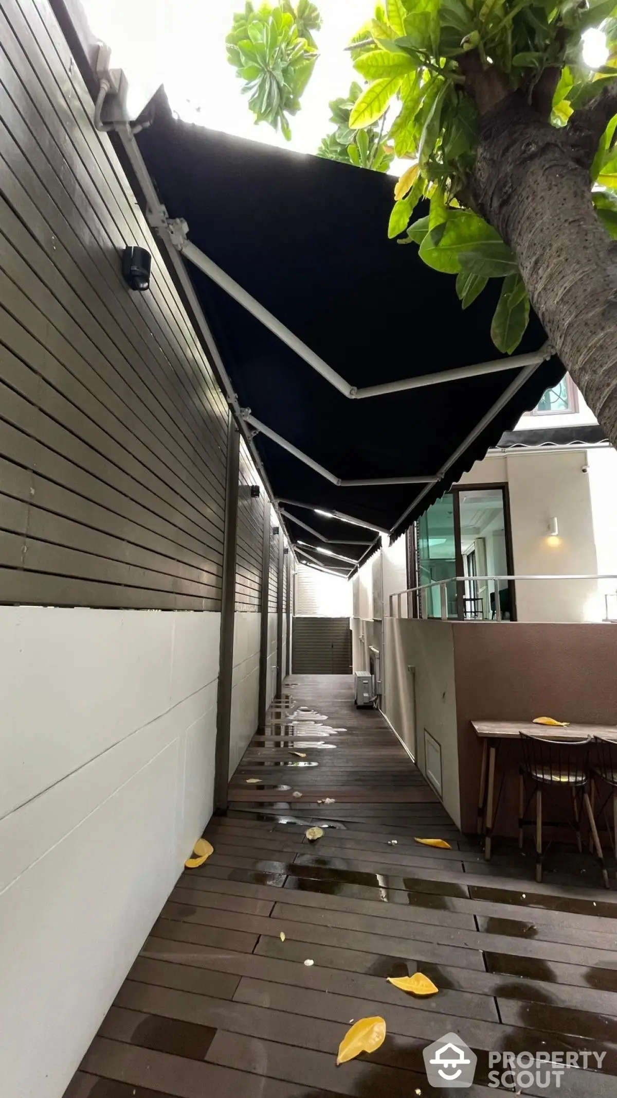 Charming outdoor walkway with modern awning and lush greenery, perfect for relaxation and outdoor dining.