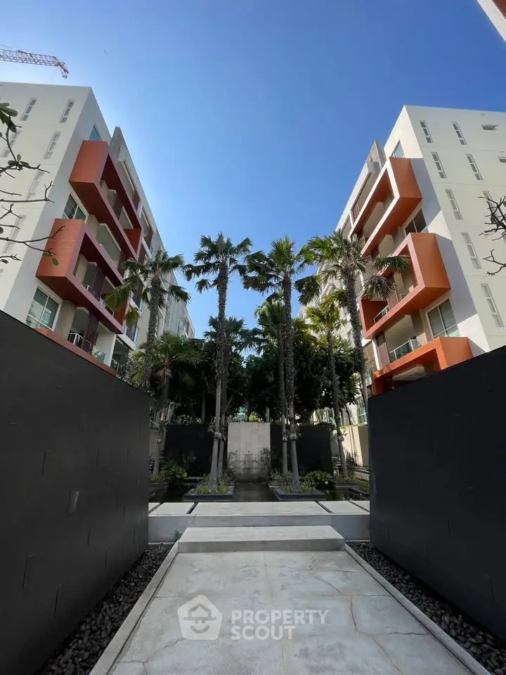 Modern apartment complex with lush garden and palm trees, showcasing contemporary architecture.
