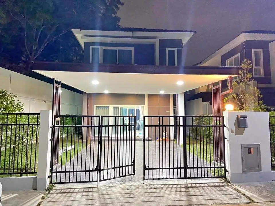 Modern two-story house with gated driveway and well-lit entrance at night.