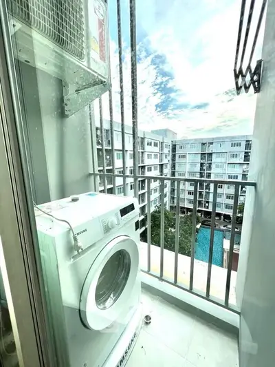 Compact balcony with washing machine and scenic view of modern apartment complex.