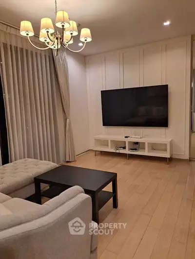 Elegant living room with modern decor, featuring a large flat-screen TV and stylish chandelier lighting.