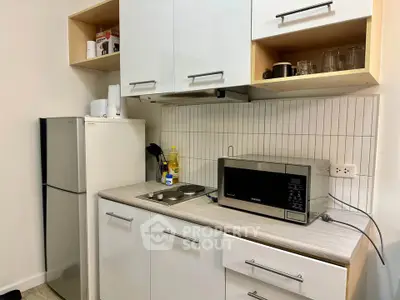 Modern kitchen with sleek cabinets, microwave, and fridge in compact layout.