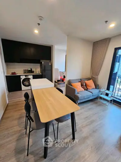 Modern open-plan living room with kitchen, featuring sleek furniture and large windows for natural light.