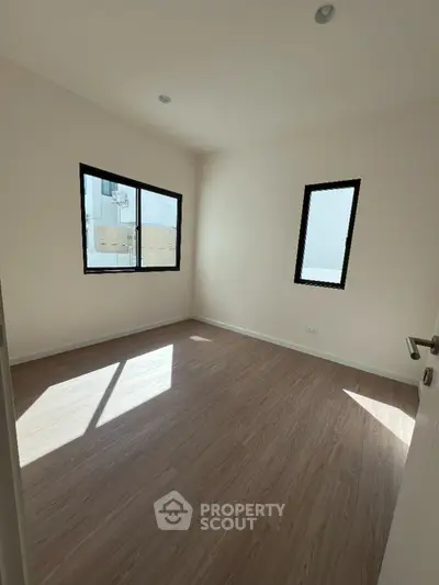 Bright empty room with wooden flooring and large windows, perfect for customization.