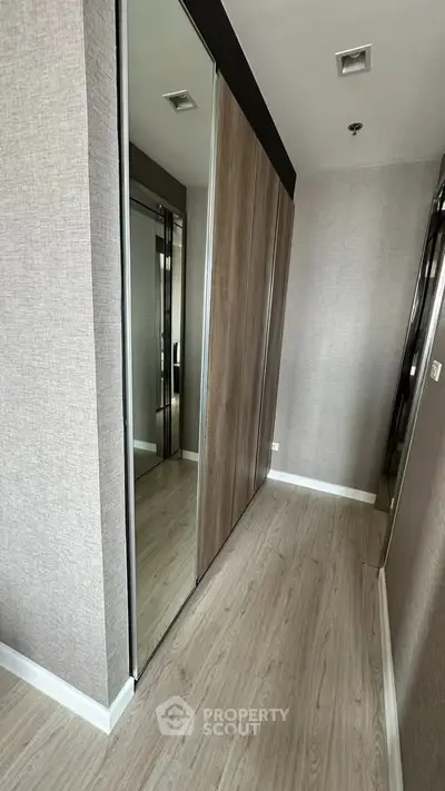 Modern hallway with mirrored closet doors and wood flooring in a stylish apartment.