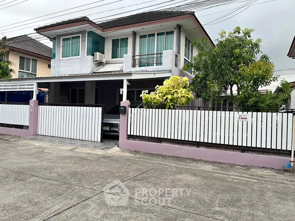Charming two-story house with gated driveway and lush greenery in a quiet neighborhood.