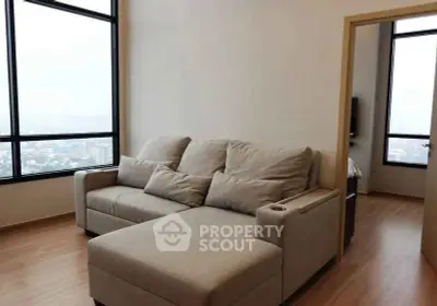 Modern living room with large windows and cozy beige sofa in high-rise apartment.