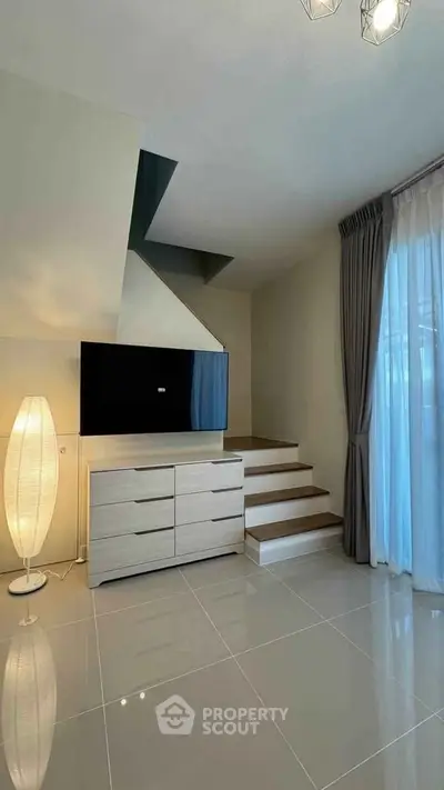 Modern living room with sleek TV setup and elegant staircase design.
