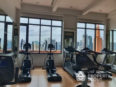 Modern gym with city view featuring treadmills and exercise bikes in high-rise building.