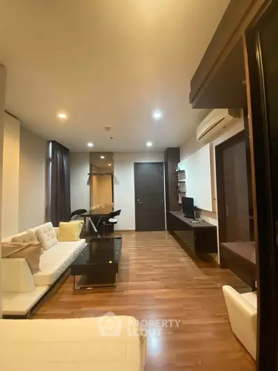 Modern living room with sleek furniture and wooden flooring, featuring a cozy workspace and ambient lighting.