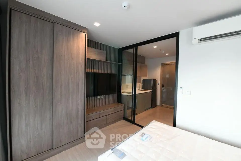 Modern bedroom with built-in wardrobe and sliding glass door to kitchen area.