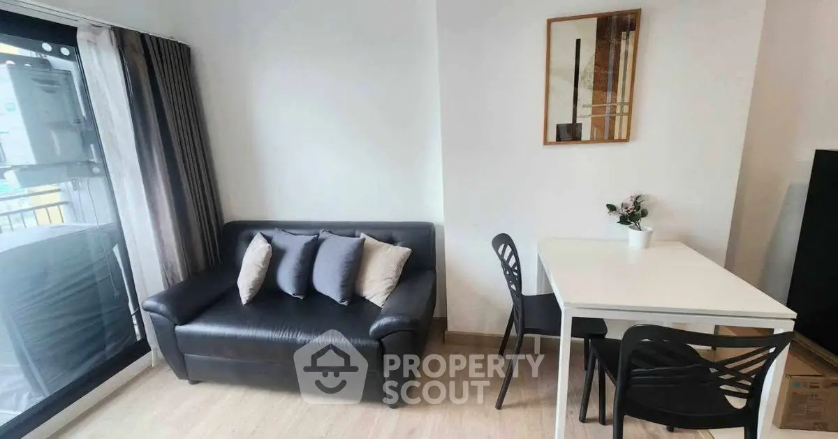 Modern living room with sleek black sofa and dining area, featuring a large window for natural light.