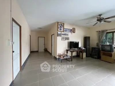 Spacious living room with tiled floor and ceiling fan, featuring a TV and framed pictures.