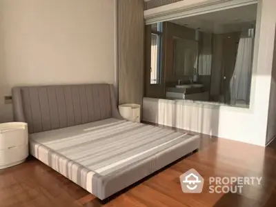 Spacious bedroom with modern design, featuring a large bed, sleek wooden flooring, and mirrored wardrobe doors reflecting natural light.