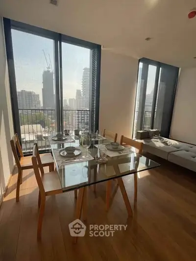 Modern dining area with glass table and city view, featuring floor-to-ceiling windows and elegant wooden flooring.