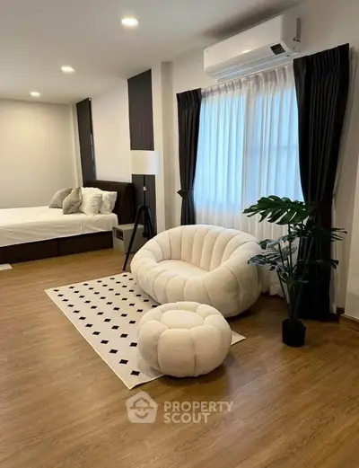 Modern bedroom with stylish furniture and elegant decor, featuring a cozy seating area and large window.