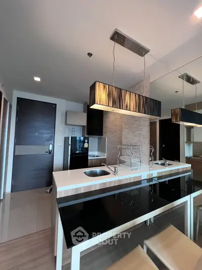 Modern kitchen with sleek design, featuring a black fridge, stylish lighting, and a breakfast bar.
