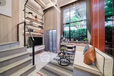 Modern living room with high ceilings, stylish staircase, and large windows offering a lush garden view.