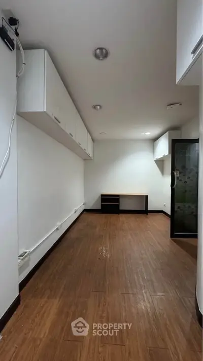 Spacious room with wooden flooring and white cabinets, ideal for office or study setup.